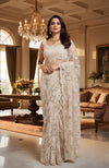 A woman in a white Chantilly lace saree and matching blouse stands in a luxurious room.